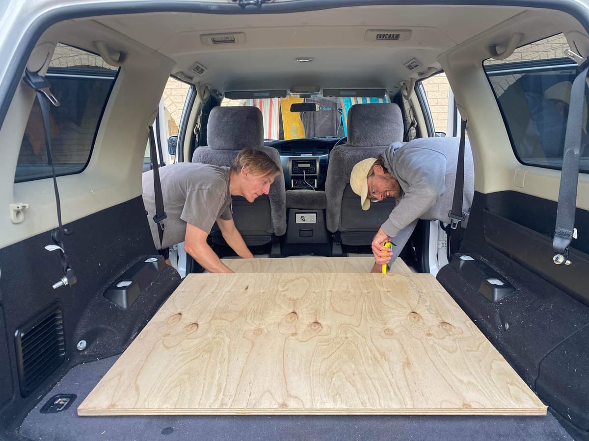 Two friends measuring and fitting a wooden board in the back of the Nissan Patrol